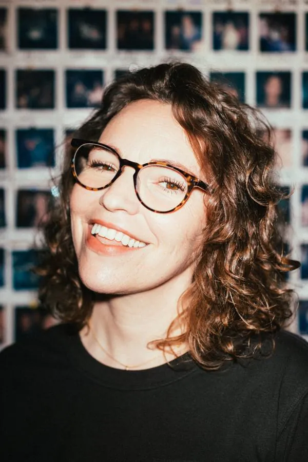 Beth smiling in front of a wall of polaroids