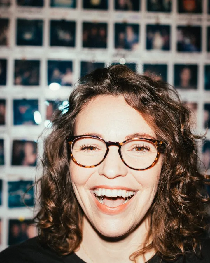 Beth laughing in glasses in front of a wall of polaroids