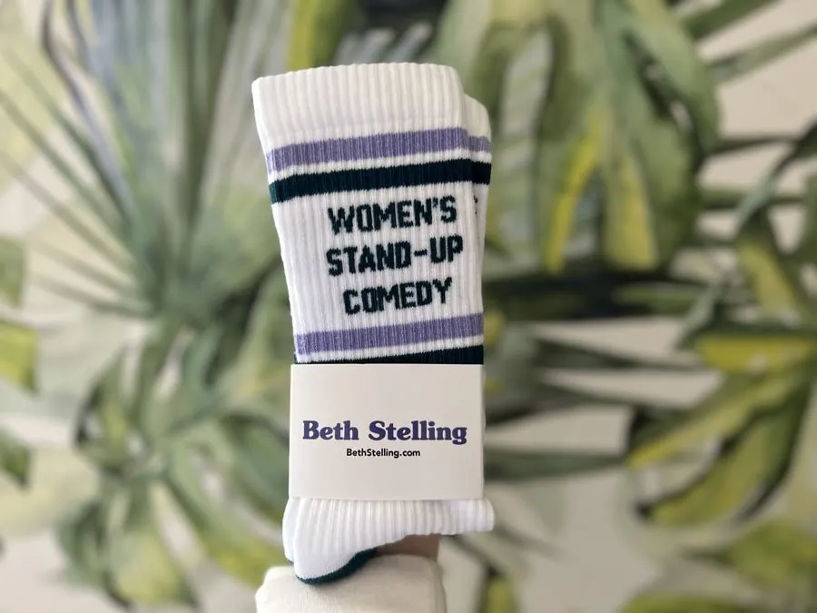 White crew socks with lavender and green stripes reading Women's Stand-up Comedy, with a Beth Stelling band