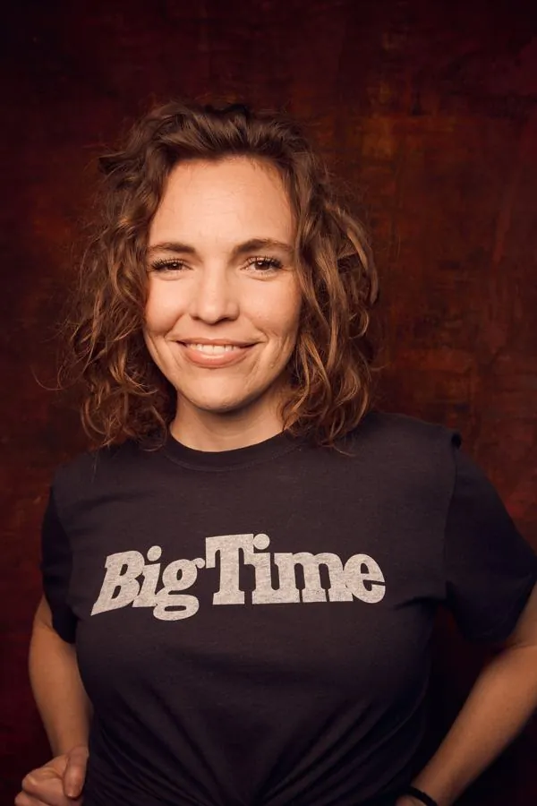Beth in a Big Time t-shirt against a dark red wall