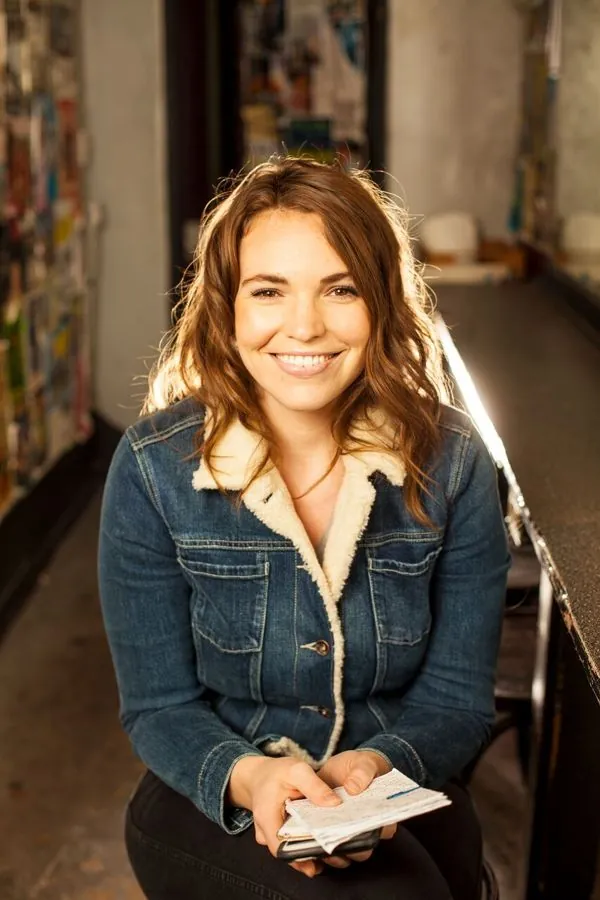 Beth in a denim jacket smiling backstage, holding a notebook
