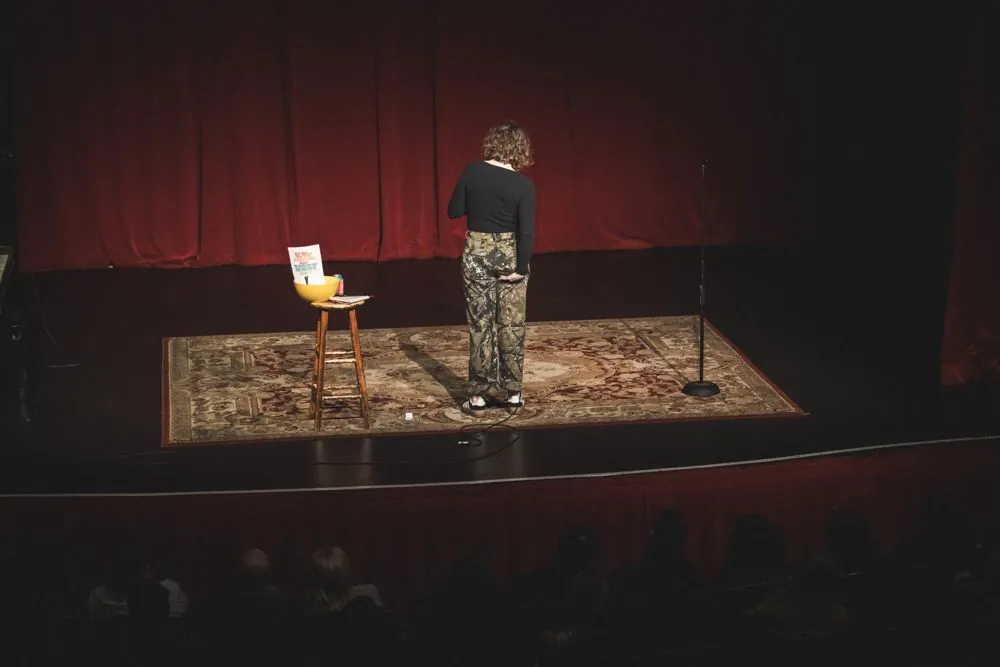 Beth on stage at Largo, a wide shot of the stage with a rug and a stool under red curtains