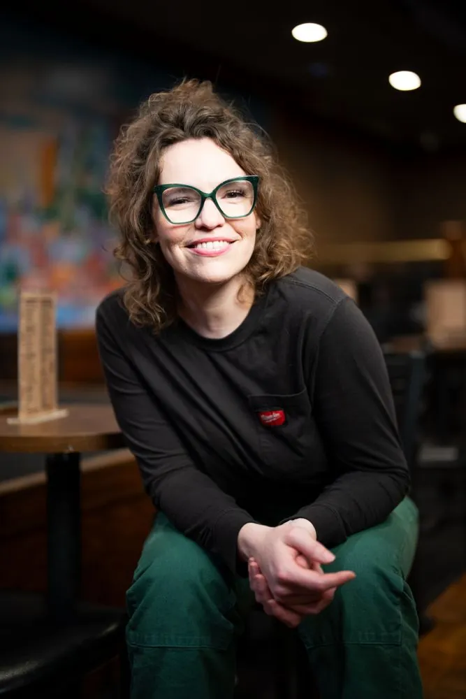 Beth in glasses sitting forward on a stool in a bar